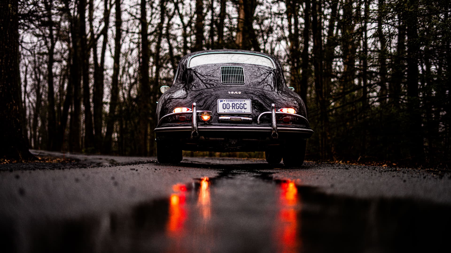 Black Porsche 356 on a wet forest road with tail light reflections