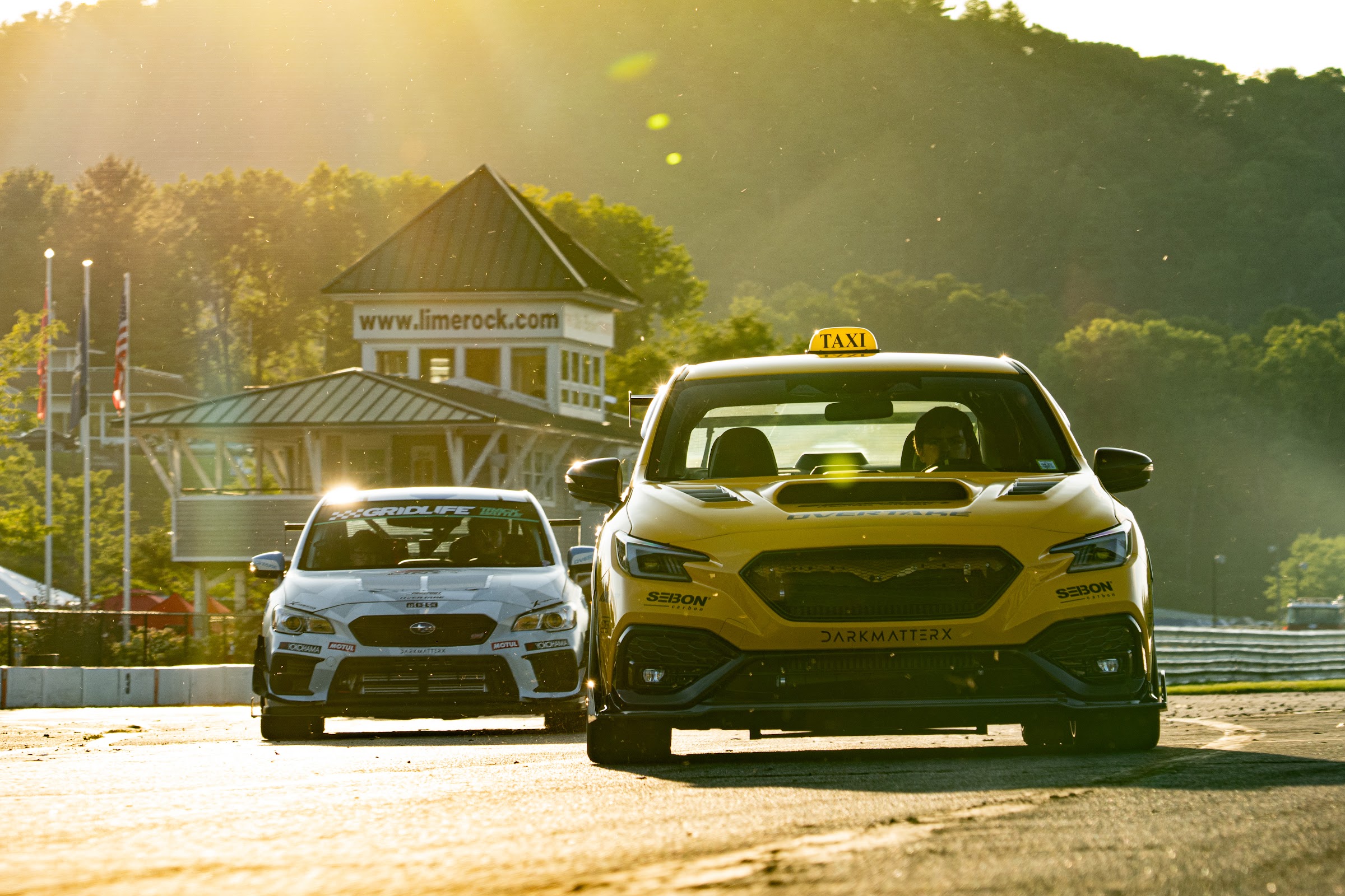 Two Subarus running side by side into a golden-hour corner